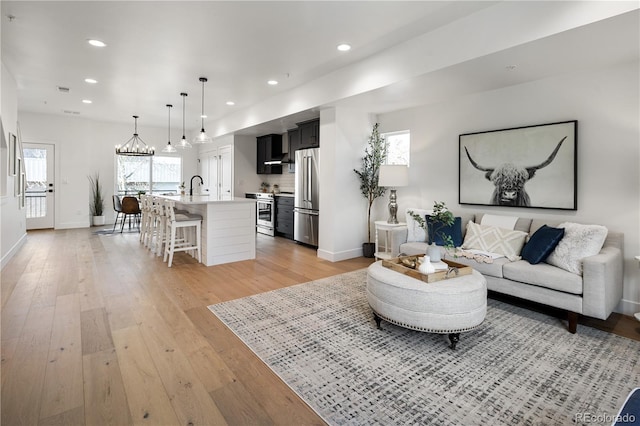living area featuring a chandelier, light wood-type flooring, baseboards, and recessed lighting