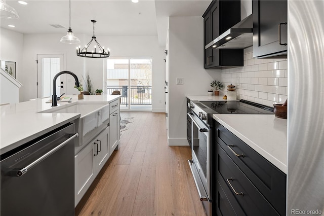 kitchen featuring wall chimney exhaust hood, visible vents, light countertops, a sink, and stainless steel appliances