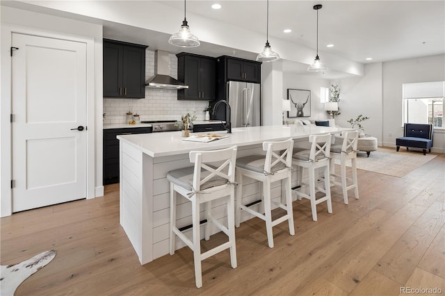 kitchen featuring wall chimney exhaust hood, light wood-style flooring, high end refrigerator, dark cabinetry, and light countertops