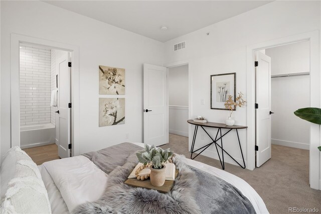 bedroom featuring baseboards, ensuite bathroom, a walk in closet, visible vents, and light colored carpet