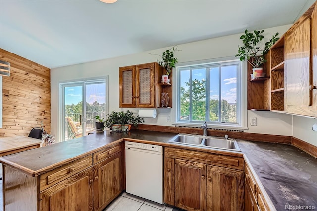 kitchen featuring sink, light tile patterned floors, dishwasher, wooden walls, and kitchen peninsula