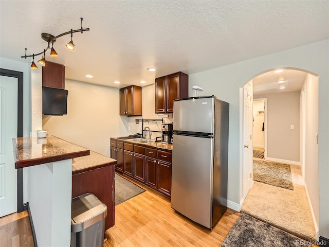 kitchen with sink, stainless steel refrigerator, light hardwood / wood-style floors, a kitchen bar, and kitchen peninsula