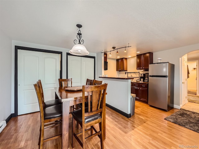 dining space featuring track lighting, a textured ceiling, and light hardwood / wood-style floors