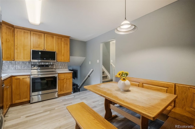 kitchen with pendant lighting, decorative backsplash, stainless steel appliances, and light hardwood / wood-style floors