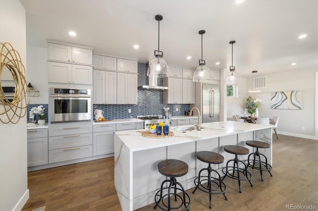 2010 Irving St, Denver, CO 80211 - kitchen with stainless steel appliances, backsplash, wall chimney exhaust hood, wood finished floors, and a kitchen bar