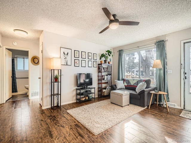 living room featuring ceiling fan, visible vents, and dark wood finished floors