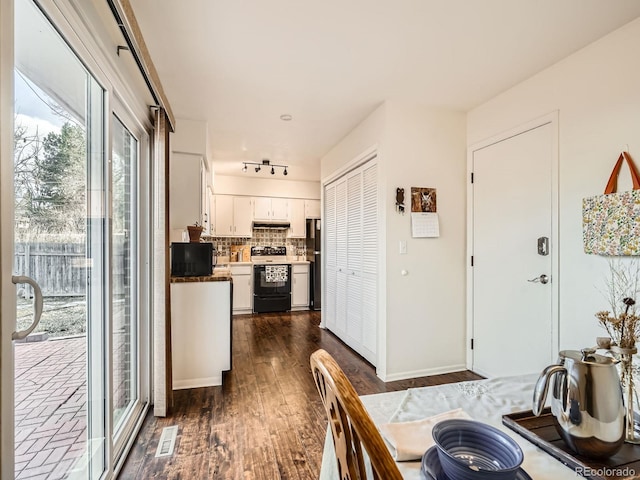 kitchen featuring dark wood-style floors, freestanding refrigerator, under cabinet range hood, white cabinetry, and range with electric stovetop