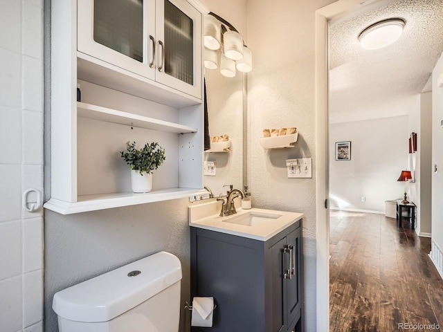 bathroom featuring a textured wall, toilet, a textured ceiling, vanity, and wood finished floors