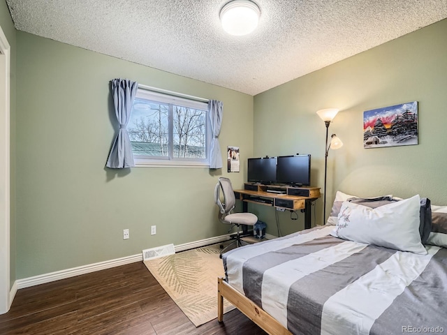 bedroom with a textured ceiling, wood finished floors, visible vents, and baseboards