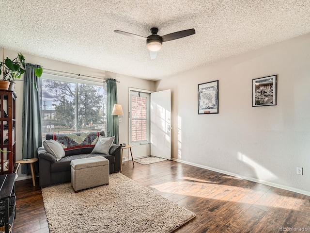 living room with wood-type flooring, ceiling fan, a textured ceiling, and baseboards