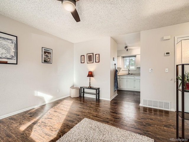 interior space with a textured ceiling, a sink, visible vents, baseboards, and wood-type flooring