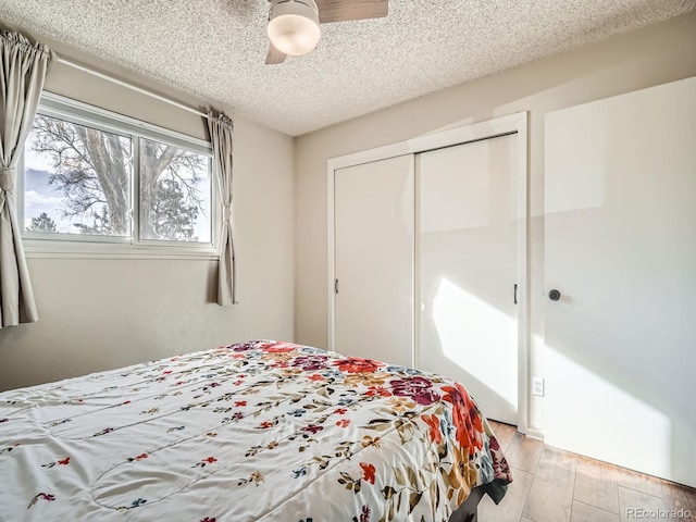 bedroom featuring a textured ceiling, light wood-style flooring, a closet, and a ceiling fan