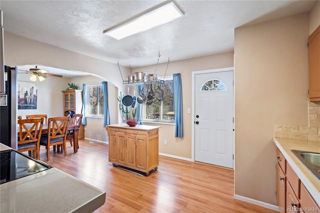 kitchen with a kitchen island, ceiling fan, light brown cabinets, a textured ceiling, and light hardwood / wood-style flooring