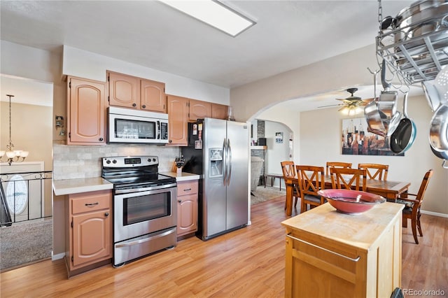 kitchen with ceiling fan with notable chandelier, pendant lighting, tasteful backsplash, light hardwood / wood-style floors, and stainless steel appliances