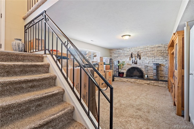 stairs featuring a stone fireplace, a textured ceiling, and carpet flooring