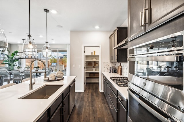 kitchen featuring dark brown cabinetry, sink, dark hardwood / wood-style floors, pendant lighting, and stainless steel appliances