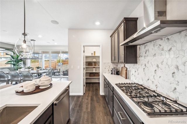 kitchen with dark brown cabinetry, wall chimney range hood, pendant lighting, stainless steel appliances, and backsplash