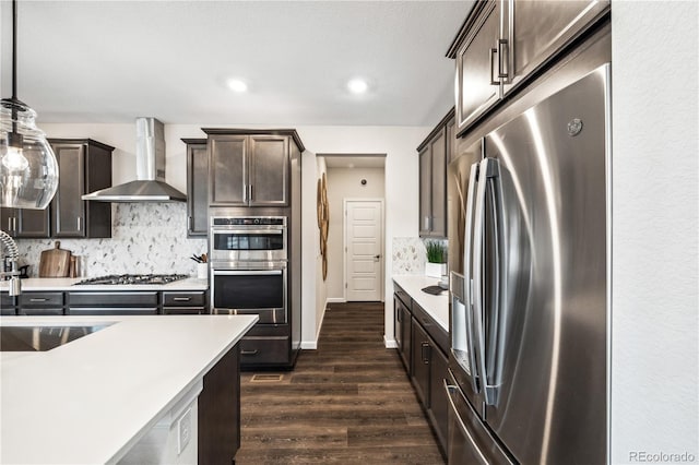 kitchen featuring appliances with stainless steel finishes, hanging light fixtures, tasteful backsplash, dark hardwood / wood-style flooring, and wall chimney exhaust hood