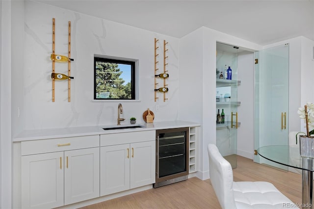 bar with beverage cooler, indoor wet bar, light wood-type flooring, and a sink