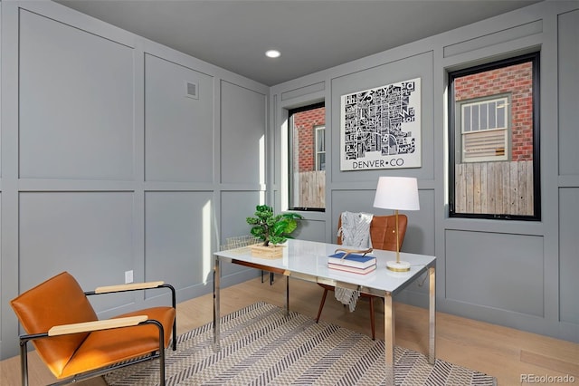 office space featuring light wood-type flooring, visible vents, and a decorative wall