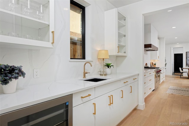 bar with a sink, ventilation hood, wine cooler, stainless steel stove, and light wood finished floors