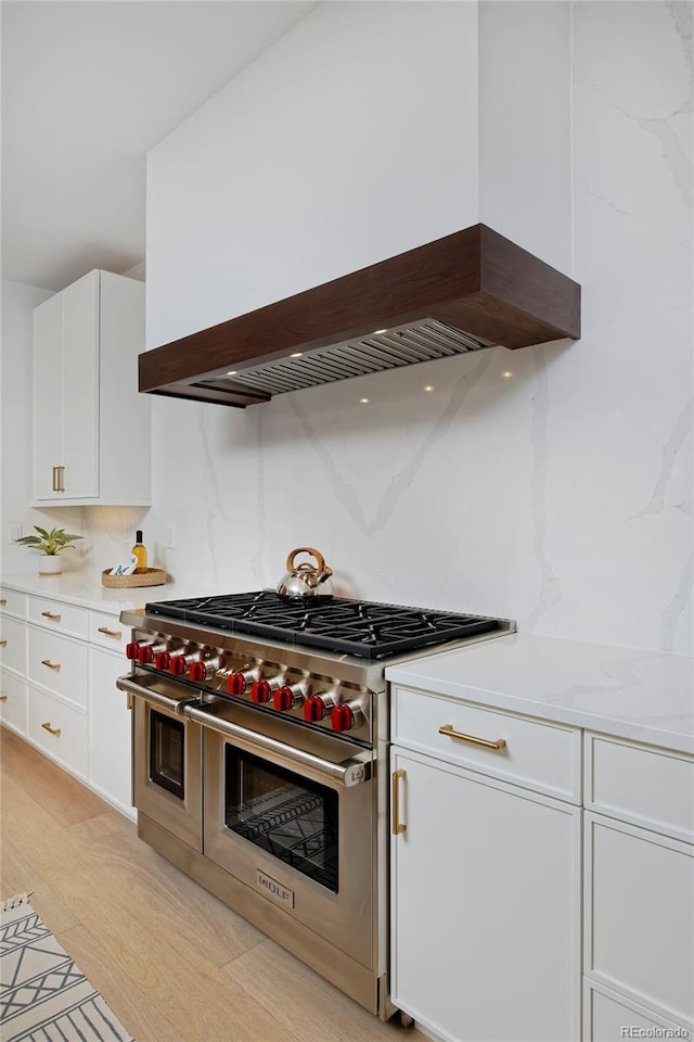 kitchen featuring double oven range, light countertops, custom range hood, white cabinets, and light wood-style floors