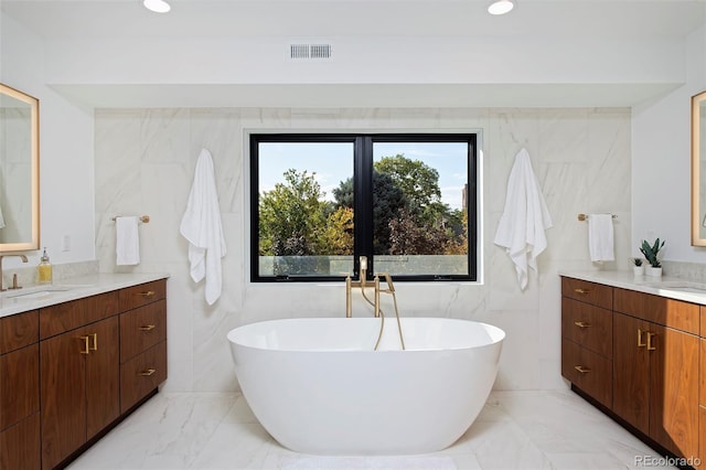 bathroom featuring visible vents, a soaking tub, two vanities, a sink, and marble finish floor