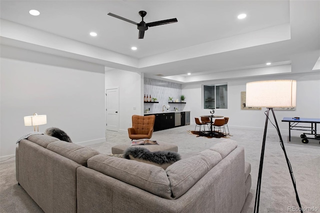 living area featuring a tray ceiling, indoor wet bar, baseboards, light colored carpet, and ceiling fan