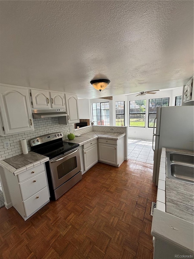 4362 Denmark Ct, Denver, CO 80239 - kitchen with stainless steel electric range oven, under cabinet range hood, a peninsula, white cabinets, and a textured ceiling
