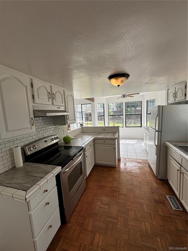 4362 Denmark Ct, Denver, CO 80239 - kitchen with electric range, under cabinet range hood, a peninsula, white cabinets, and decorative backsplash