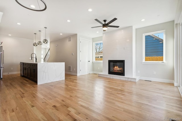 unfurnished living room with a tiled fireplace, ceiling fan, and light hardwood / wood-style flooring