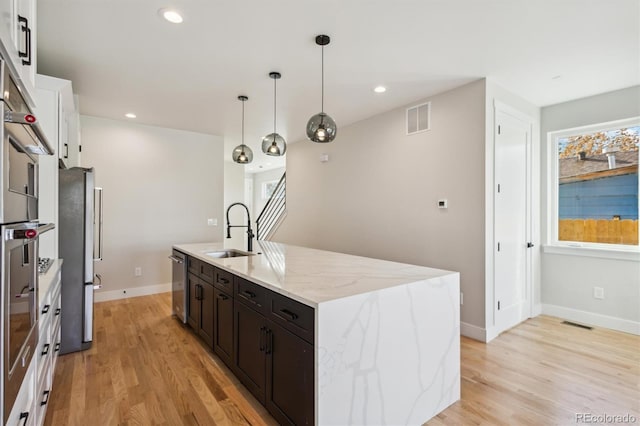 kitchen featuring pendant lighting, a kitchen island with sink, sink, light stone countertops, and stainless steel appliances