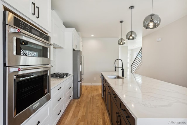 kitchen with appliances with stainless steel finishes, sink, white cabinets, light hardwood / wood-style floors, and an island with sink