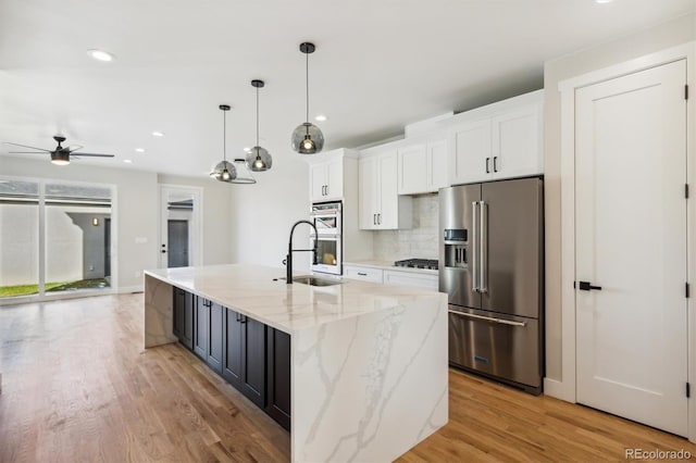 kitchen with a kitchen island with sink, sink, light hardwood / wood-style flooring, appliances with stainless steel finishes, and white cabinetry