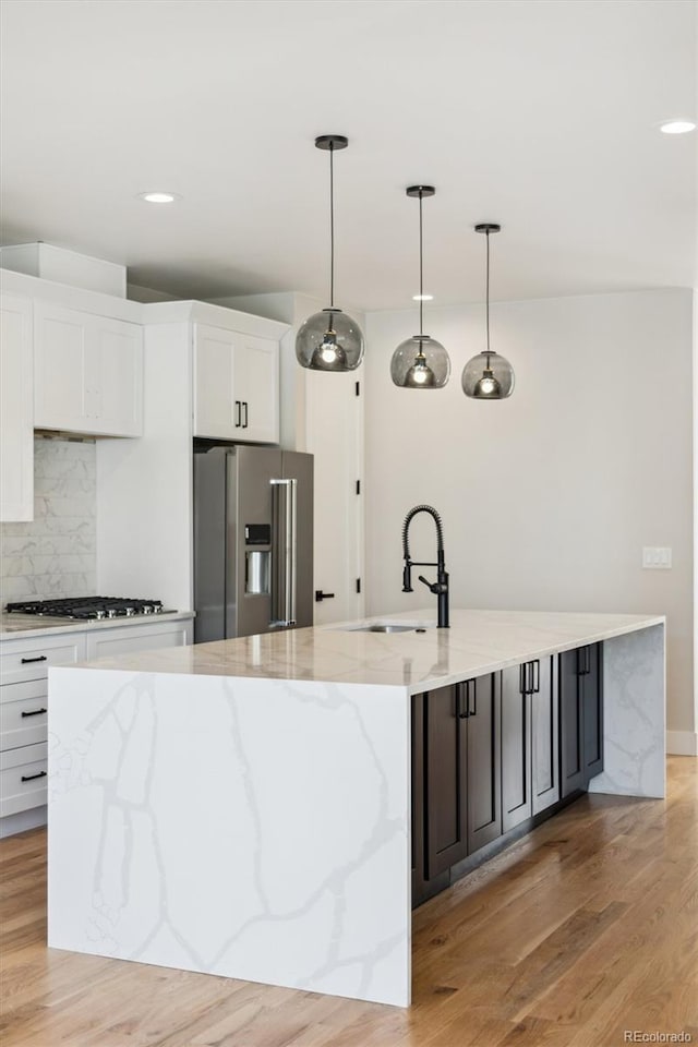 kitchen featuring white cabinets, stainless steel appliances, hanging light fixtures, and light hardwood / wood-style flooring