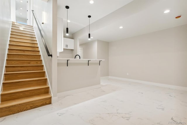 interior space featuring white cabinetry, sink, kitchen peninsula, decorative light fixtures, and a kitchen bar