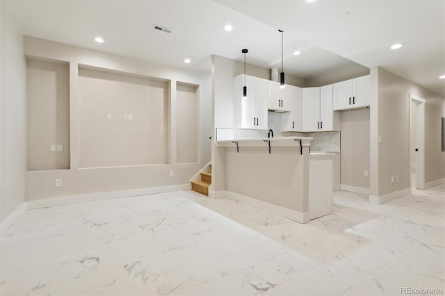 kitchen featuring a kitchen bar, kitchen peninsula, tasteful backsplash, white cabinets, and hanging light fixtures