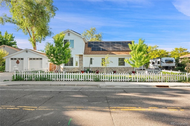 traditional-style house with a fenced front yard, stone siding, a garage, concrete driveway, and solar panels