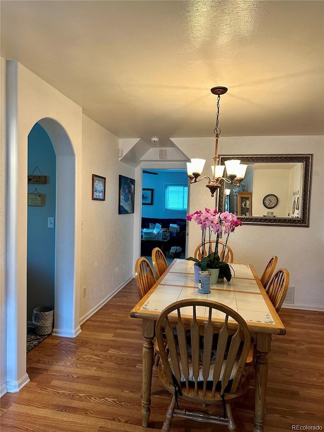 dining room featuring an inviting chandelier, arched walkways, baseboards, and wood finished floors