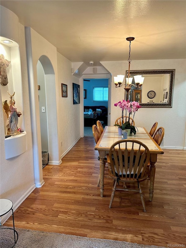 dining space featuring baseboards, arched walkways, a textured wall, and wood finished floors