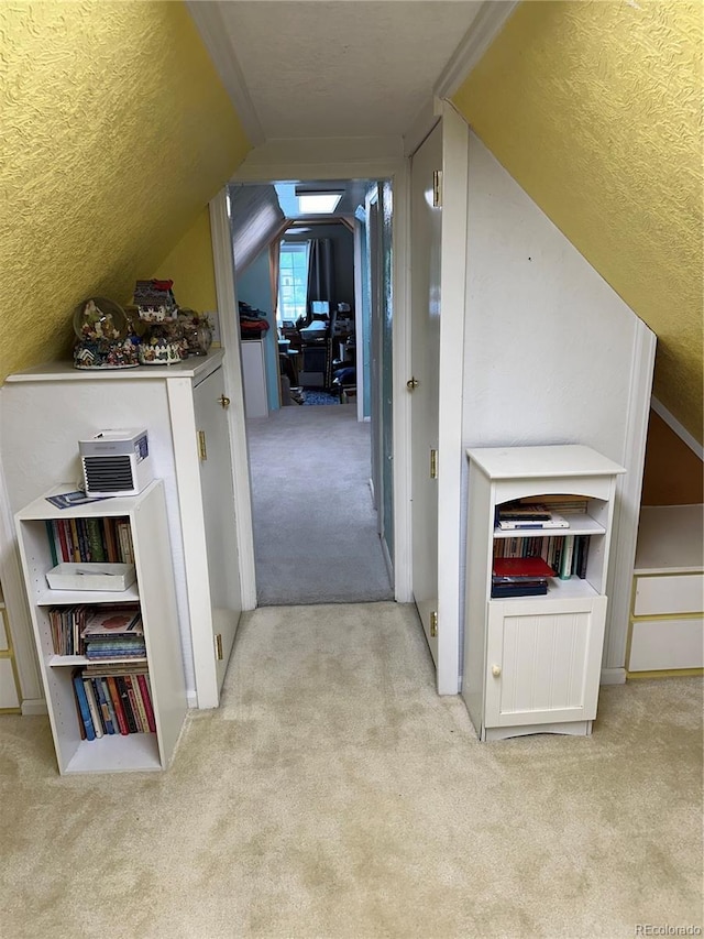 hallway featuring light carpet, vaulted ceiling, and a textured ceiling