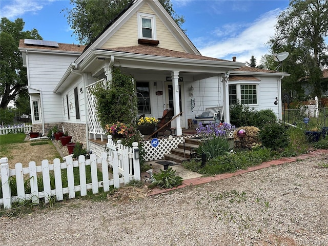 bungalow with covered porch, fence private yard, roof mounted solar panels, and roof with shingles