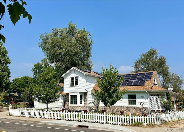 view of front of house featuring a shingled roof, a fenced front yard, solar panels, and stone siding