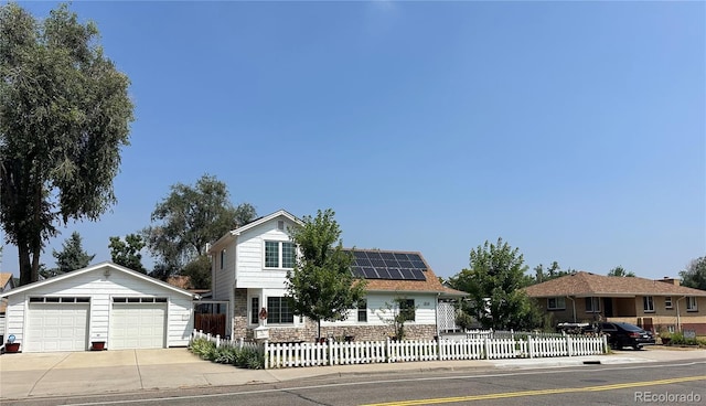traditional-style house with an outdoor structure, a garage, stone siding, roof mounted solar panels, and a fenced front yard