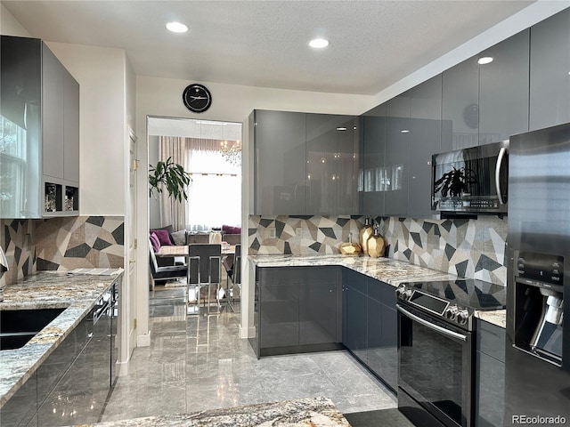 kitchen featuring modern cabinets, gray cabinets, light stone counters, stainless steel appliances, and decorative backsplash