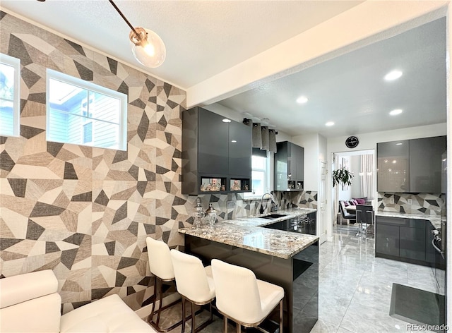 kitchen with a breakfast bar, light stone counters, recessed lighting, modern cabinets, and a sink