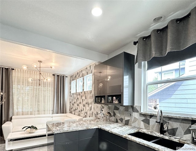 kitchen featuring light stone countertops, a chandelier, a sink, hanging light fixtures, and decorative backsplash