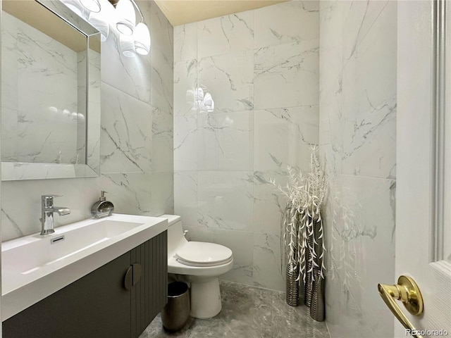 bathroom featuring toilet, vanity, marble finish floor, and tile walls