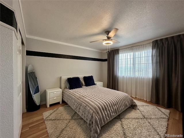 bedroom featuring ornamental molding, ceiling fan, a textured wall, a textured ceiling, and light wood finished floors