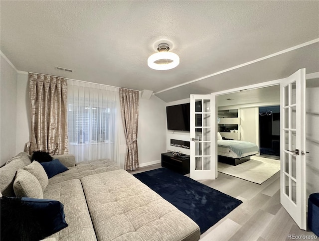 bedroom featuring visible vents, a textured ceiling, wood finished floors, vaulted ceiling, and french doors